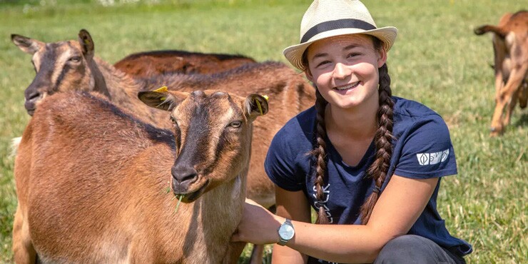 Schulbauernhof Zukunftsfelder: Eine Jugendliche auf einem grünen Feld umgeben von Ziegen