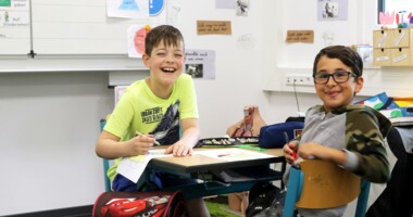 Zwei Jungs in ihrem Klassenraum lachen in die Kamera.
