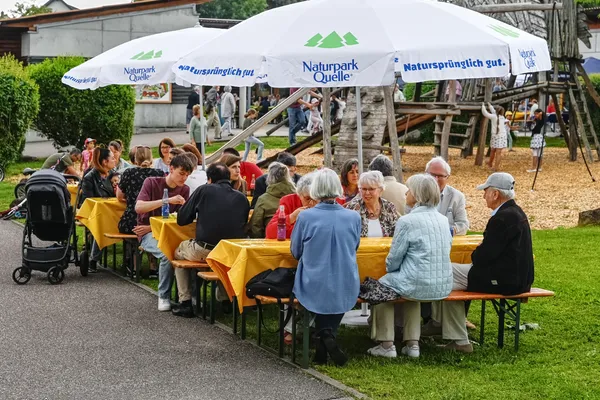 Menschen sitzen beim Jahresfest an Tischen und Bänken zusammen